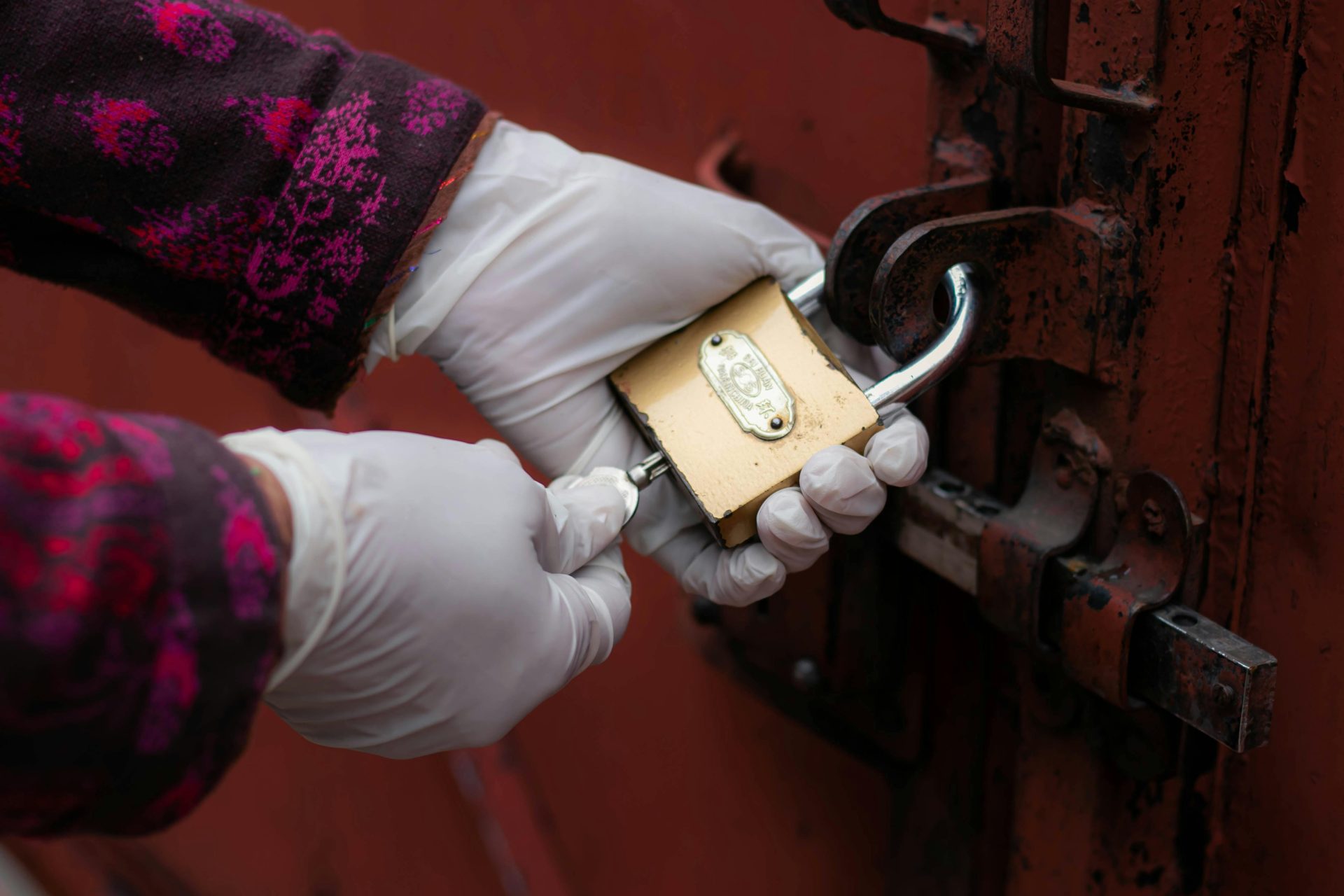 Gros plan sur des mains gantées déverrouillant un cadenas de porte rouillé.